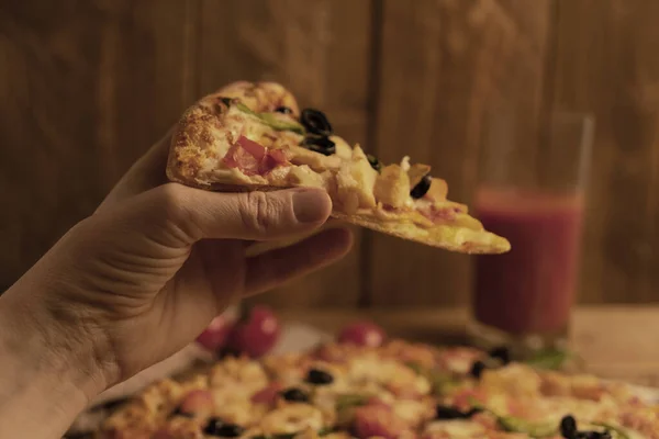 Bir kadın elindeki lezzetli pizzayı ahşap arka planda tutuyor.