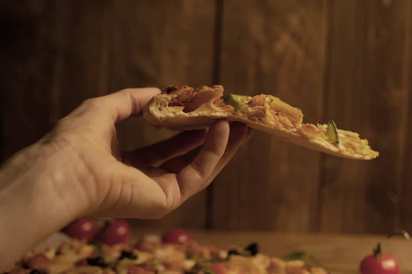 Bir kadın elindeki lezzetli pizzayı ahşap arka planda tutuyor.