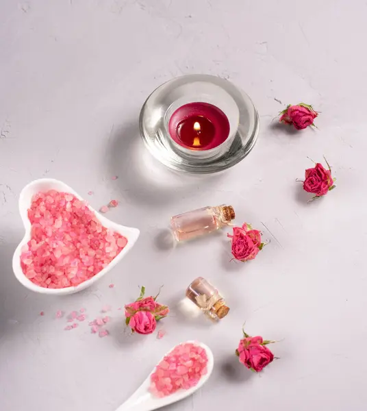 Spa terapisi, küçük gül çiçekleri, mum ve gri arka planda aromatik yağ.