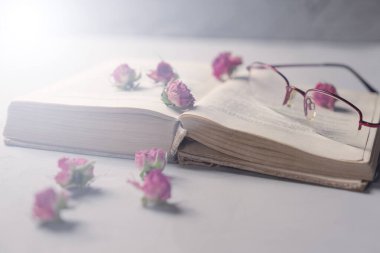 Açık bir kitap, okuma bardakları ve masada kuru çiçekler.