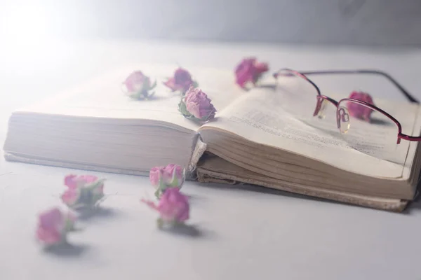 Açık bir kitap, okuma bardakları ve masada kuru çiçekler.