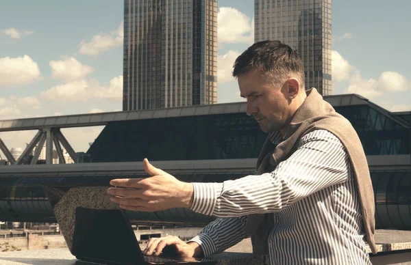 A young man businessman works on a laptop outdoors in the business center of Moscow City in the summer