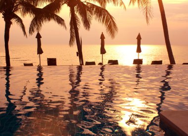 Günbatımı ve palmiye ağaçları havuzda.