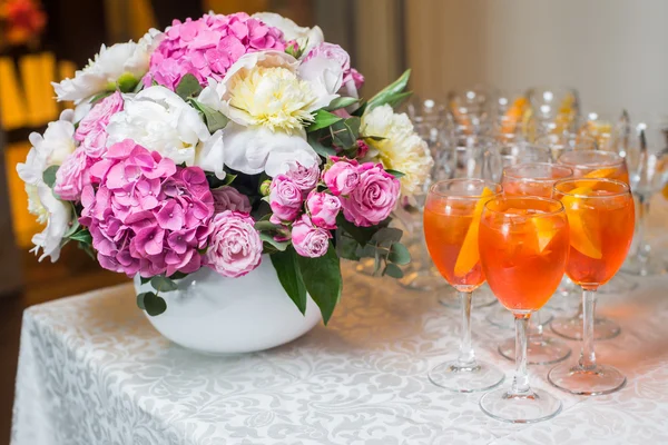 Orange exotic cocktail served at the table with a bouquet of flo — Stock Photo, Image