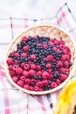 Raspberries and blueberries in a straw vase on a table cloth