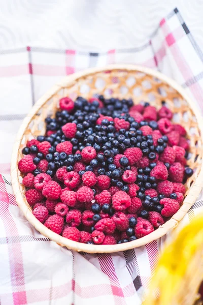 Raspberries and blueberries in a straw vase on a table cloth — Φωτογραφία Αρχείου