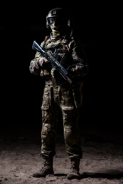 Soldier in camouflage with a rifle standing on a platoon and watches — Stock Photo, Image