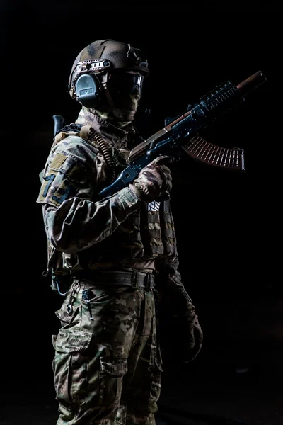 Soldado equipado em pé no perfil e segurando máquina automática levantada — Fotografia de Stock