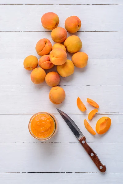 Свежие абрикосы и кусочки абрикоса на деревянном столе с ножом — стоковое фото