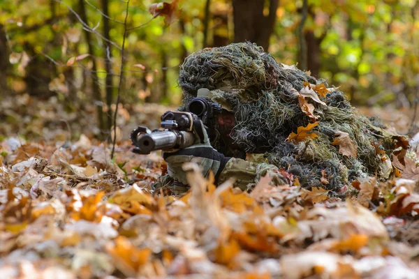 Francotirador se encuentra entre las hojas caídas en el bosque — Foto de Stock