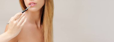 Genç bir kadın fırçayla ruj sürüyor.