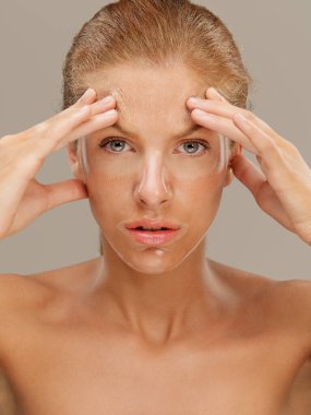 Yüzünde maske olan güzel sarışın bir kadının yakın plan güzel portresi, elleriyle yüzünü çerçeveliyor, kaşlarını çatıyor.