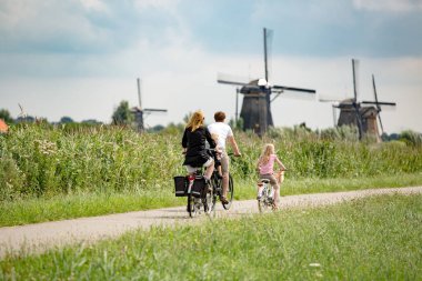 Hollanda Kinderdijk - 14 Haziran: İki çocuklu mutlu aile, Kinderdijk UNESCO Dünya Mirası yakınlarındaki bir ara sokakta bisiklet sürüyor. 14 Haziran 2015 'te Hollanda Kinderdijk' te.