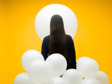 Sarı arka planda beyaz balonları olan uzun saçlı genç bir esmer.