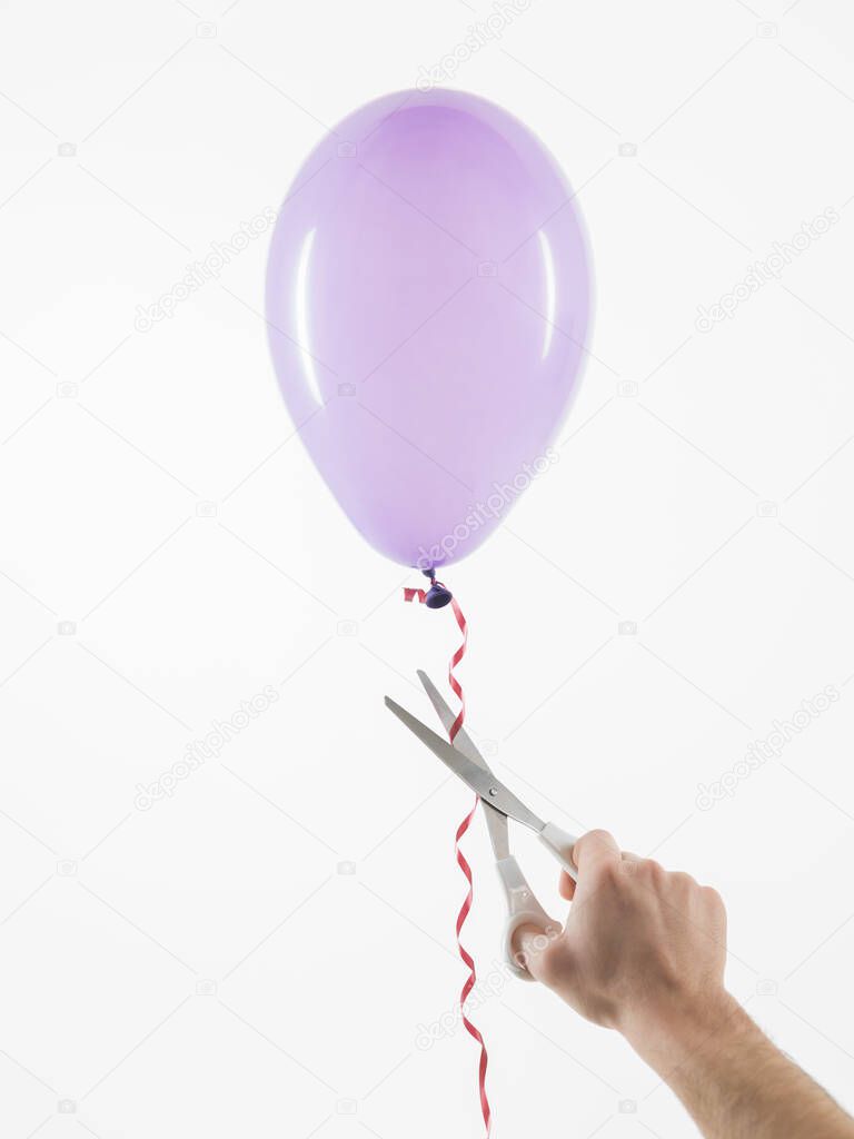 male hand using scissors to free a purpleballoon, white background, concept