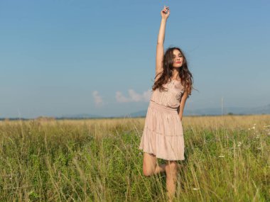 Saçında çiçeklerle yeşil tarlada duran, kameraya gülümseyen güzel genç bir kadın.