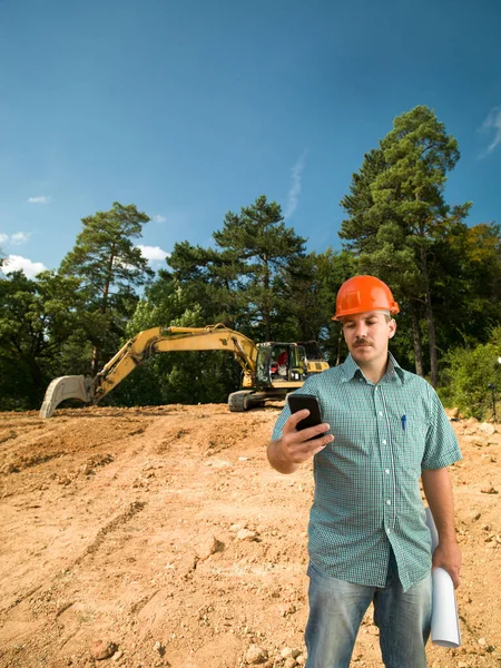 Ingeniero Mirando Teléfono Móvil Sosteniendo Planos Sitio Construcción — Foto de Stock