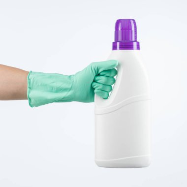 İnsan eli koruyucu eldiven takıyor, çamaşır deterjanı kabını beyaz arka planda tutuyor.