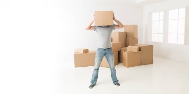 Kafasını karton kutuya saklayan bir adam, yeni bir dairede duruyor, umutsuzluk jesti