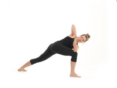 Siyah giyinmiş, beyaz arka planda genç bir kadının zor dengeli yoga pozunu sergilemesi