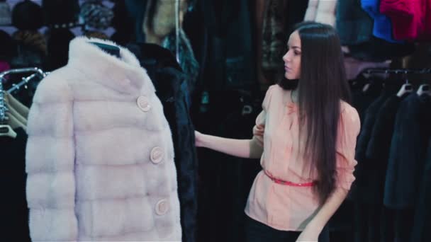 Hermosa chica de cabello castaño elige un abrigo de piel en la tienda. Compras. Serie . — Vídeos de Stock