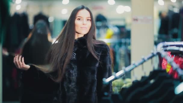 Hermosa chica de cabello castaño elige un abrigo de piel en la tienda. Compras. Serie . — Vídeos de Stock