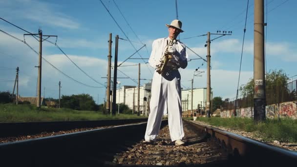 Saxofonista, homem, homem de meia-idade em pé sobre os dormentes ferroviários. Série . — Vídeo de Stock