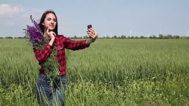 Mujer joven morena con un ramo de flores silvestres hace selfie . — Vídeo de stock