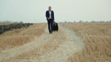 İş takım elbiseli bir adam ile bir seyahat çantası hasat buğday sahaya geliyor..