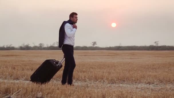Un uomo in giacca e cravatta viene fornito con una borsa da viaggio su un campo di grano raccolto . — Video Stock