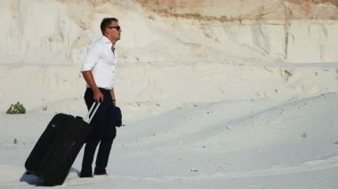 Çölde bir iş adamı. Genç bir adam bir takım elbise ve bir büyük Bagaj çanta çölde. İşadamı tatil için yolda. Beyaz kum. Bunaltıcı çöl.