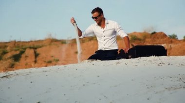 Kum üzerine oturan bir Bagaj çanta ile iş takım elbiseli bir genç adam. Strewed kum parmaklarımın arasından