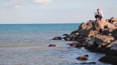 Denizde büyük kayalar üzerine oturan işadamı ve dizüstü bilgisayar için iş yok. Uzaktan çalışma, serbest.