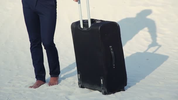 Affärsman i öknen. En ung man i kostym och en stor bagage väska i öknen. Affärsman på vägen till resorten. Vit sand. Kvav öknen. — Stockvideo