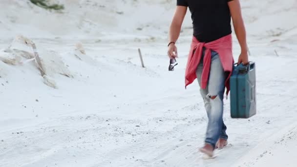 Un joven atraviesa el desierto con un bote de gasolina en busca de combustible . — Vídeos de Stock