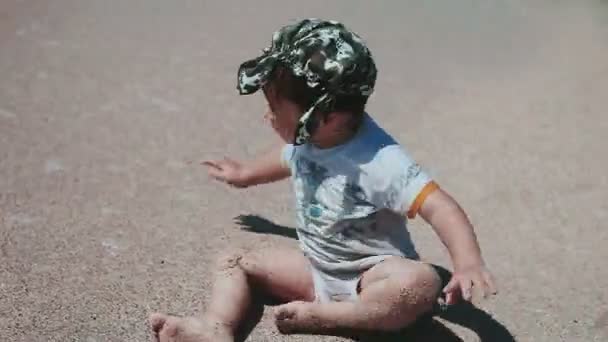 Niño de 2 años de edad, aspecto hermoso, jugando en la arena en la orilla del mar. La ropa mojada y divertida. Día de verano junto al mar . — Vídeos de Stock