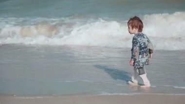 Erkek Yaşı 2 yıl eski, güzel görünüm, kum sahil üzerinde oynamak. Islak giysileri ve eğlenceli. Yaz günü deniz tarafından.