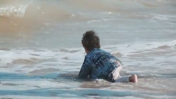 Niño de 2 años de edad, aspecto hermoso, jugando en la arena en la orilla del mar. La ropa mojada y divertida. Día de verano junto al mar . — Vídeo de stock