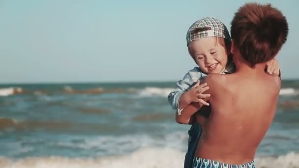 Dois irmãos. O irmão mais velho segura seu irmão mais novo em seus braços na praia. Uma família . — Vídeo de Stock