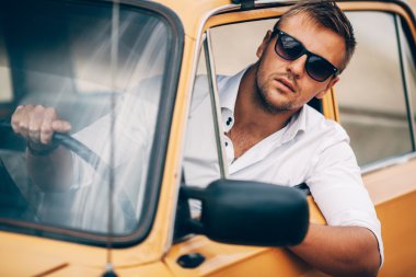 Genç adam bir güzel görünüm retro arabanın direksiyonuna.