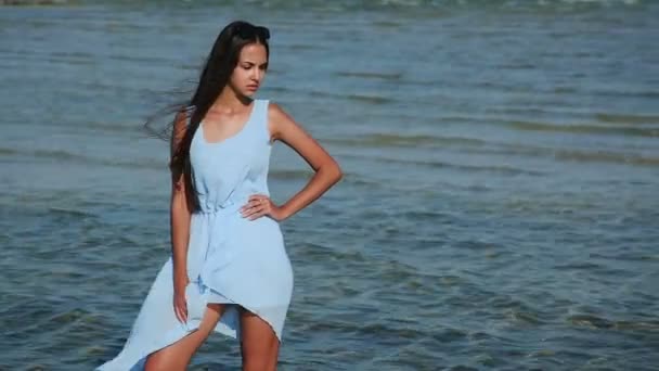 Belle fille attrayante est venue à la plage et est allée dans l'eau. Une fille qui marche sur la plage. Fille en robe bleue et est allé à la mer. Des éclaboussures d'eau . — Video