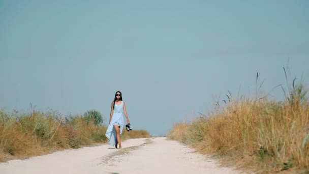 Стройная девушка идет по песчаной дороге к пляжу — стоковое видео