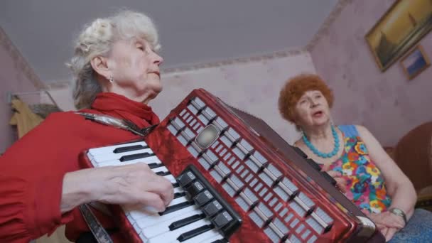 Senior mujer juega acordeón mientras amigo canta en la habitación — Vídeos de Stock