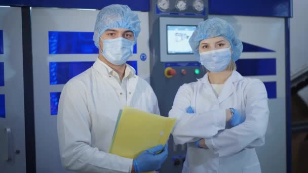 Чоловік і жінка в уніформі і маски стоять біля нового обладнання — стокове відео