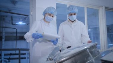İşçi fabrikada üretim hattını kadın müfettişe gösteriyor