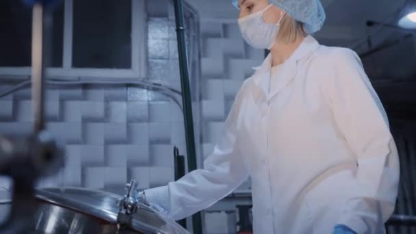 Una mujer que lleva una máscara protectora abre la tapa de un tanque de metal en una planta de procesamiento de alimentos — Vídeos de Stock