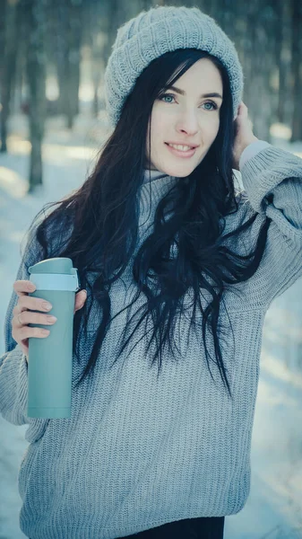 Kış ormanlarında elinde termo bardakla genç bir kadın.