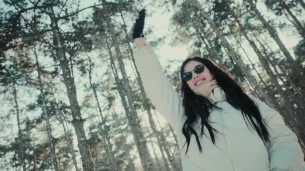 Lycklig kvinna med solglasögon vågor hand i vinterskogen — Stockvideo