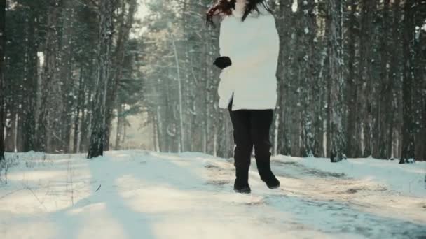 Mulher de jaqueta branca corre ao longo da estrada nevada na floresta de inverno — Vídeo de Stock