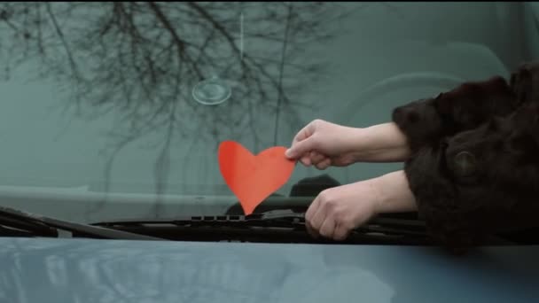 La chica deja secretamente un corazón de papel bajo el parabrisas de su coche novios — Vídeos de Stock